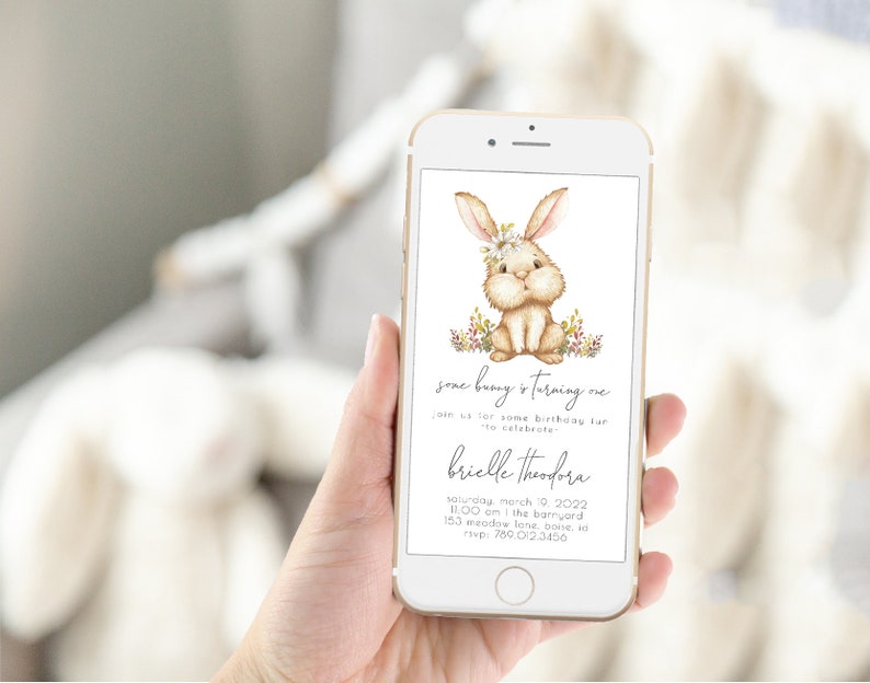 May include: A digital invitation for a first birthday party with a cute cartoon bunny wearing a flower crown. The invitation says "Some bunny is turning one" and includes the name "Brielle Theodora", the date "Saturday, March 19, 2022", the time "11:00 am", the location "The Barnyard, 153 Meadow Lane, Boise, ID", and the phone number "780.012.3456".