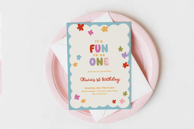 May include: A colorful invitation for Olivia's 1st birthday, featuring the text "It's FUN to be ONE" in playful, multi-colored letters. The invitation is decorated with flower illustrations and sits on a pink plate with a white envelope.