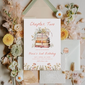 May include: A white invitation card with a pink floral border. The card features a stack of books with a pink ribbon and a floral arrangement on top. The text "Chapter Two" is in pink at the top of the card. The text "Olivia's 2nd Birthday" is in pink below the books. The text "SAT APRIL 16 | 6PM" is in black below the birthday text. The text "OLIVER'S HOUSE | BOOK LANE, BOISE, ID" is in black below the date and time. The text "RSVP to Olivia's Mom" is in black at the bottom of the card.