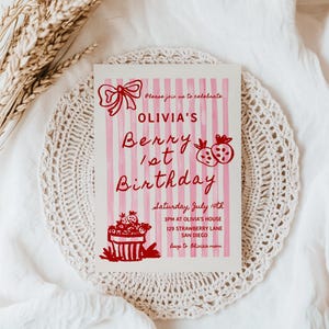 May include: Pink and white striped birthday invitation with red text that says "Olivia's Berry 1st Birthday". The invitation includes details for the party, including the date, time, and location.