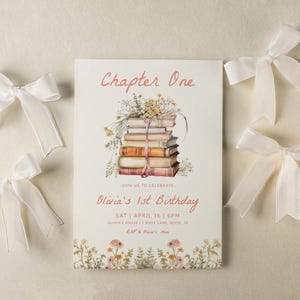 Może przedstawiać: Różowa i biała karta zaproszenia z akwarelową ilustracją stosu książek i tekstem "Chapter One" i "Olivia's 1st Birthday".