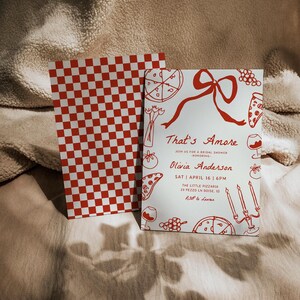 May include: A white invitation card with red text and illustrations of pizza, wine glasses, and candles. The text reads "That's Amore" and "Join us for a bridal shower honoring Olivia Anderson". The date and time of the event are listed as "Sat April 16 | 6pm" and the location is "The Little Pizzaria 29 Pezzo Ln Boise, ID". The RSVP information is "RSVP to Lauren".