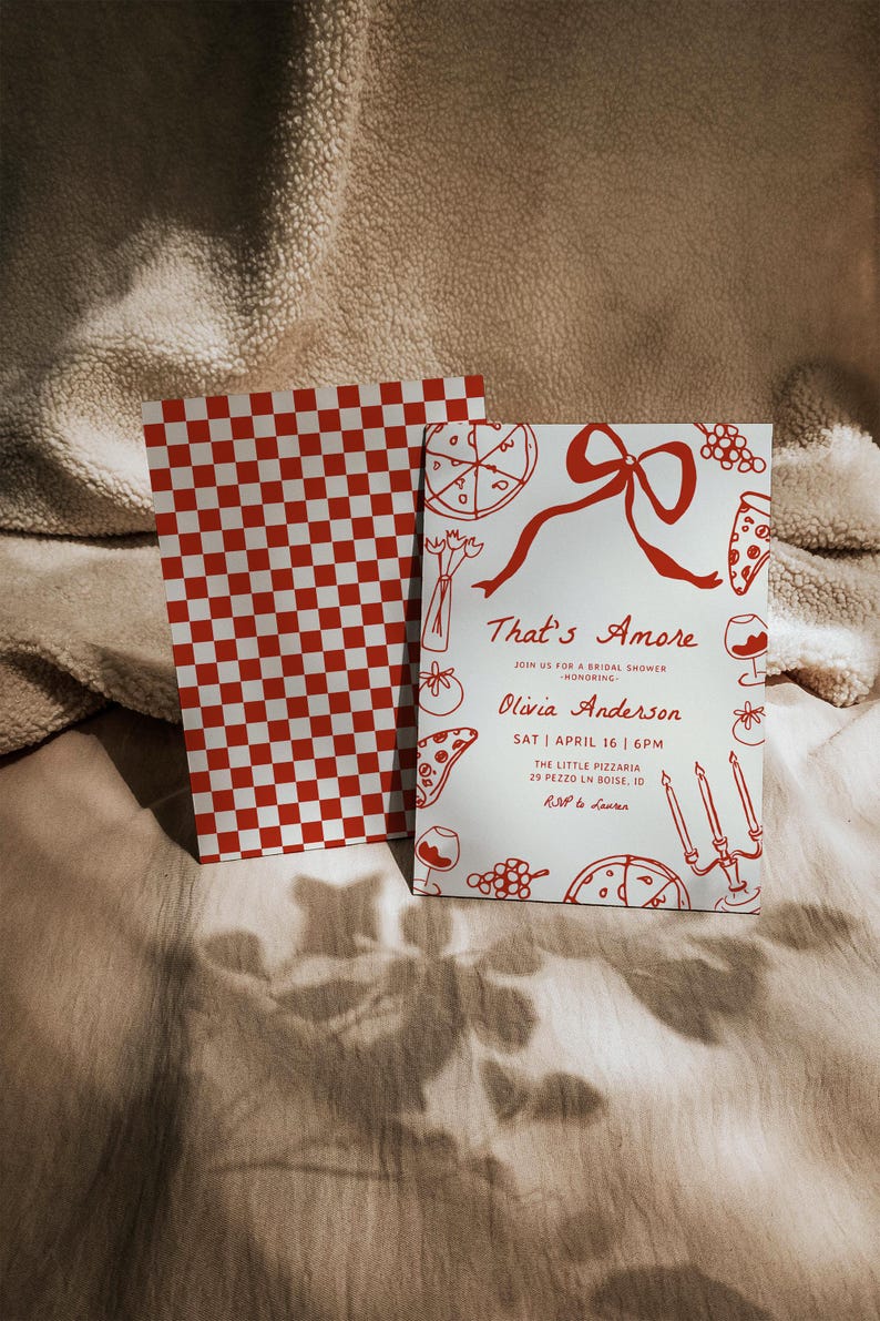 May include: A white invitation card with red text and illustrations of pizza, wine glasses, and candles. The text reads "That's Amore" and "Join us for a bridal shower honoring Olivia Anderson". The date and time of the event are listed as "Sat April 16 | 6pm" and the location is "The Little Pizzaria 29 Pezzo Ln Boise, ID". The RSVP information is "RSVP to Lauren".