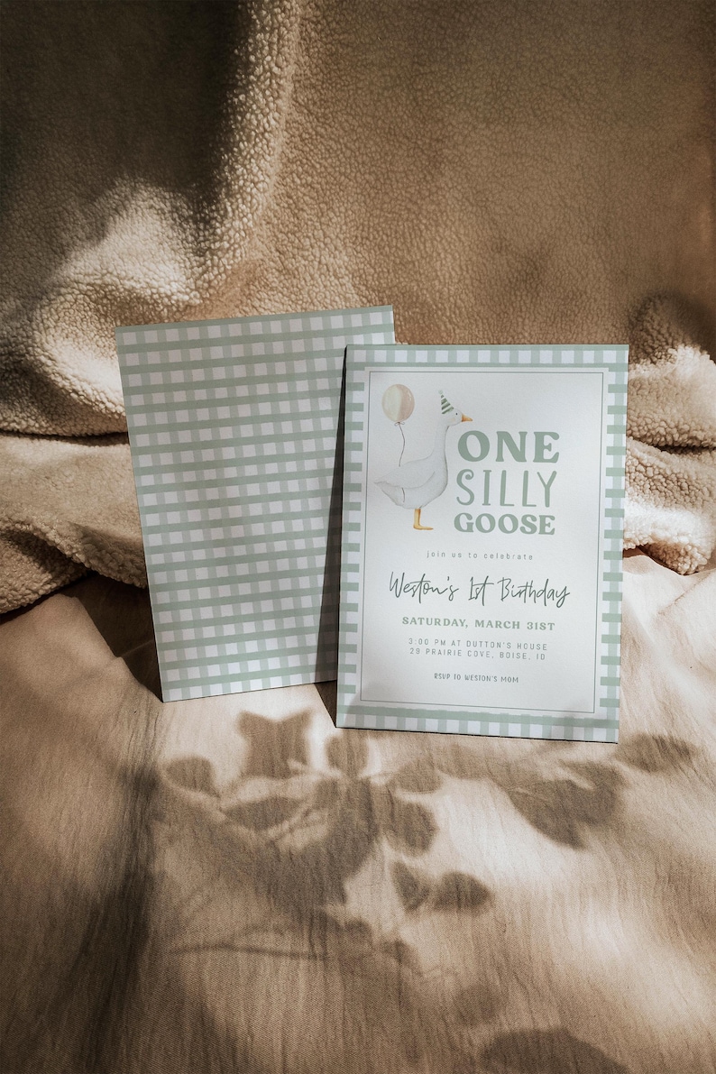 May include: An invitation with a light green and white gingham pattern, featuring the text "ONE SILLY GOOSE" and "Weston's 1st Birthday". The design includes a cartoon goose with a balloon. The invitation rests on a beige surface.