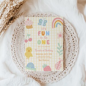 May include: A pastel yellow birthday invitation with the text "it's FUN to be ONE" and illustrations of a cupcake, butterfly, rainbow, cherry, chick, snail, strawberry, and ladybug. The invitation is for Norah's 1st birthday.