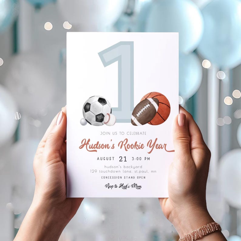 May include: A white invitation card with a blue number one and watercolor illustrations of a soccer ball, baseball, football, and basketball. The text on the card reads "Join us to celebrate Hudson's Rookie Year, August 21, 3:00 PM, Hudson's backyard, 129 Touchdown Lane, St. Paul, MN, Concession Stand Open, Rwp to Hud's Mom."