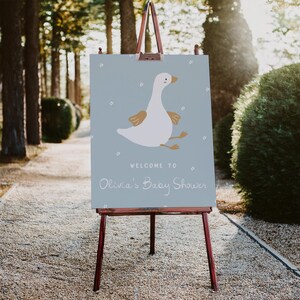 May include: A blue welcome sign with a white goose illustration and the text "Welcome to Olivia's Baby Shower".