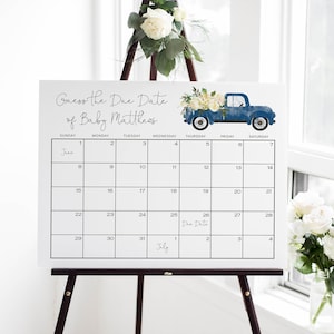 May include: A white calendar with a blue truck graphic and floral accents. The calendar is set up for June and July with the text "Guess the Due Date of Baby Matthews" at the top. The due date is marked on the calendar as July 26th.