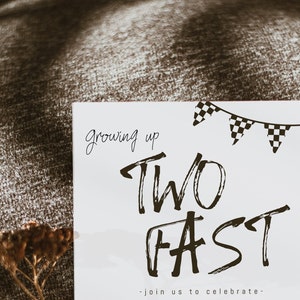 May include: A white card with black text that reads "Growing up Two Fast - Join us to celebrate."  The card has a black and white checkered banner at the top.