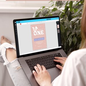 Puede incluir: Una persona usando una computadora port&aacute;til para editar una invitaci&oacute;n de primer cumplea&ntilde;os con tem&aacute;tica de conejito rosa y blanco. La invitaci&oacute;n presenta el texto "Some Bunny is One" y una linda ilustraci&oacute;n de conejito.