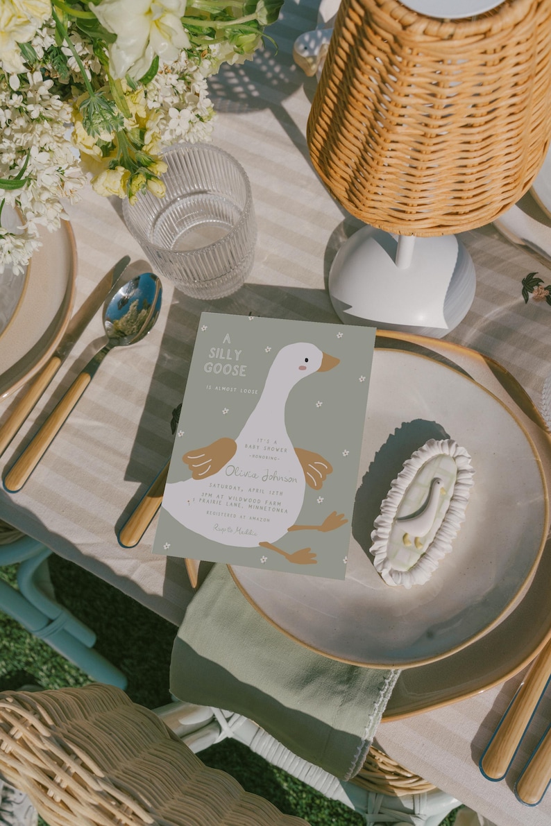 Op de afbeelding: Een baby shower uitnodiging met een cartoon gans op een groene achtergrond. De uitnodiging zegt "A Silly Goose" en bevat de naam "Olivia Johnson" en de datum "Saturday, April 15th".