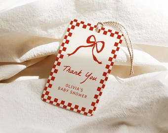 Op de afbeelding: Een rechthoekig cadeaulabel met een rood-witte geblokte rand en een rode strikillustratie. Op het label staat "Thank You" en "Olivia's Baby Shower" in rood script. Er is een natuurlijke touwtje bevestigd.