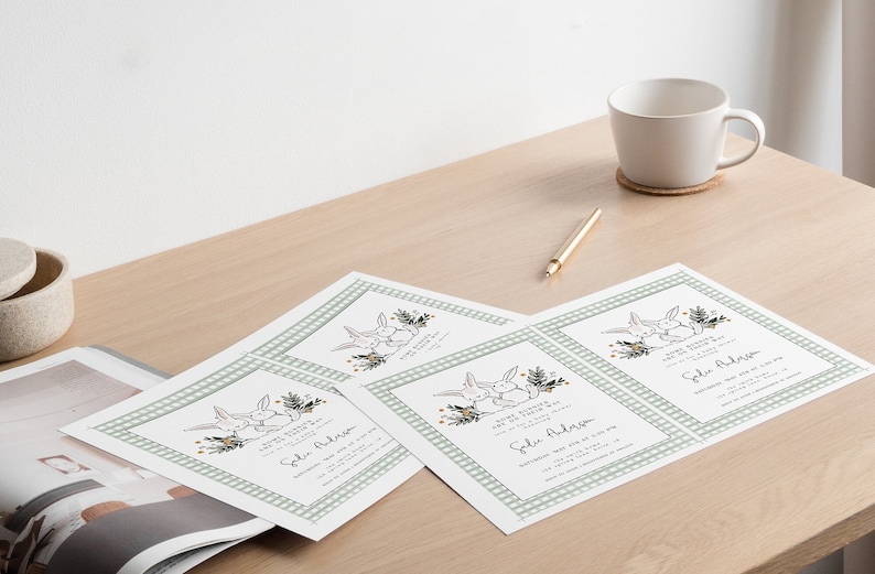 May include: Four white cards with a green and white checkered border. Each card features a drawing of two bunnies with a floral design and the text "We're having a baby shower!" and "[Name] Address".