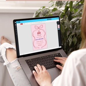 Op de afbeelding: Een persoon gebruikt een laptop om een roze en rode verjaardagsuitnodiging te bewerken met een taart- en strikdesign. De uitnodiging luidt "Doe met ons mee om te vieren" en "30e verjaardag".