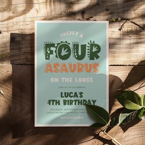 May include: A birthday party invitation with a light teal background and a dinosaur theme. The text reads "There's a Four-asaurus on the Loose" and "Luca's 4th Birthday". The invitation is on a wooden surface.