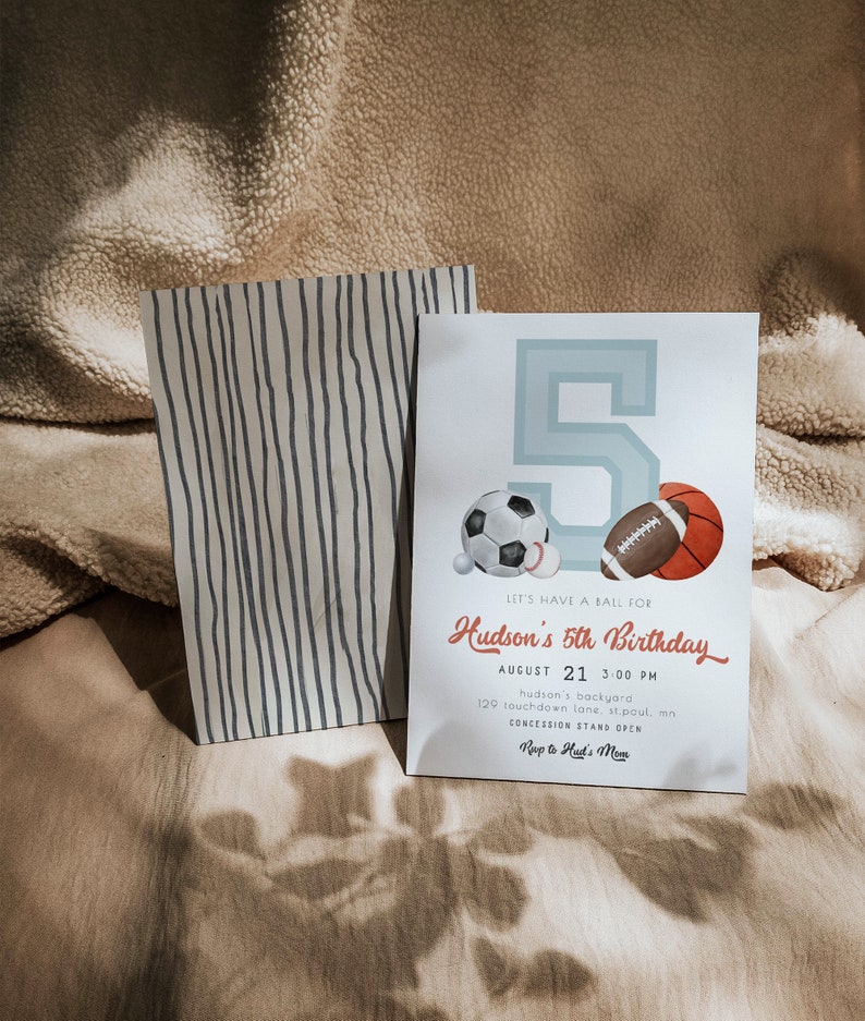 May include: A birthday invitation with a light blue number 5 and sports ball illustrations. The invitation includes the text "Let's have a ball for Hudson's 5th Birthday" and event details. A striped paper bag is next to the invitation.