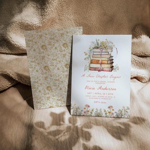 May include: A white invitation card with a floral border and a stack of books with flowers on top. The text on the card reads "A New Chapter Begins" and "Olivia Anderson".