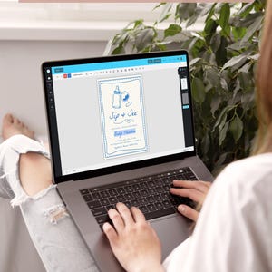 May include: A laptop screen displaying a baby shower invitation template with blue and white illustrations of a baby bottle and a wine glass. The text on the invitation reads "Sip & See" and "Baby Theodore".
