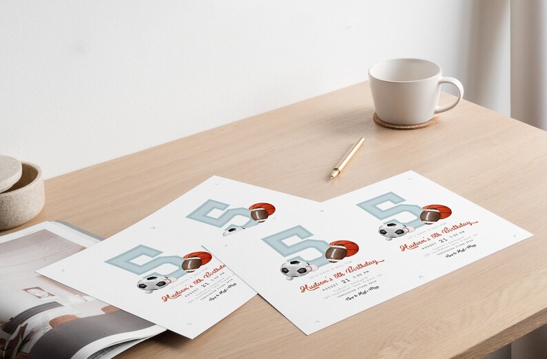 May include: Four printed invitations for a fifth birthday party, featuring a large blue number 5, a football, a soccer ball, and a basketball. The invitations are on a wooden table, with a white mug, a pen, and a coaster.