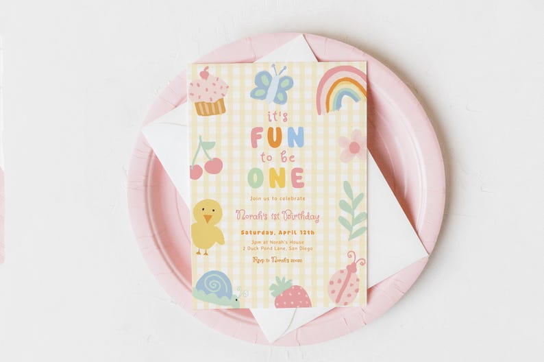 May include: A pastel-colored birthday invitation with the text "It's FUN to be ONE" on a yellow gingham background. The invitation includes illustrations of a cupcake, butterfly, rainbow, and other cute graphics. It rests on a pink plate.