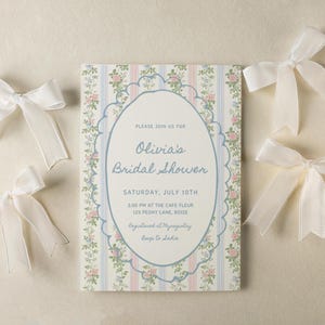 May include: A white invitation with a floral pattern and blue accents. The invitation is for Olivia's bridal shower on Saturday, July 10th at 3:00 PM at the Cafe Fleur, 129 Peony Lane, Boise. The invitation also includes the text "Registered at Myragistry" and "Beep to ladie".