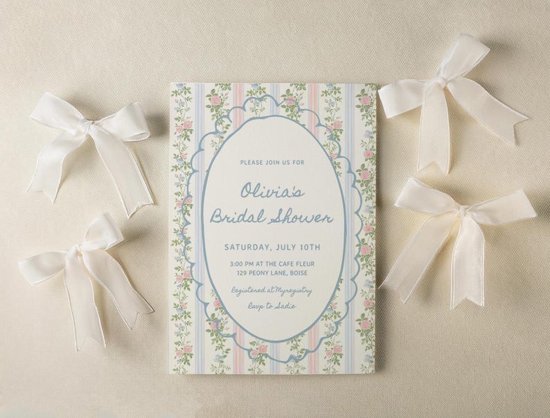 May include: A white invitation with a floral pattern and blue accents. The invitation is for Olivia's bridal shower on Saturday, July 10th at 3:00 PM at the Cafe Fleur, 129 Peony Lane, Boise. The invitation also includes the text "Registered at Myragistry" and "Beep to ladie".