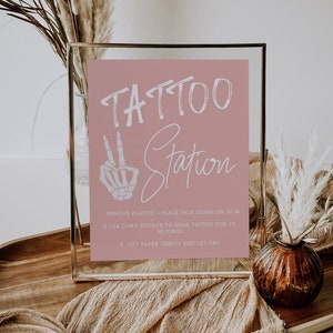 Puede incluir: Un cartel con marco dorado, fondo rosa y texto blanco que dice "TATTOO Station". El cartel incluye instrucciones para aplicar tatuajes temporales: 1. Quitar el pl&aacute;stico - Colocar la cara hacia abajo sobre la piel. 2. Usar una esponja h&uacute;meda para remojar el tatuaje durante 30 segundos. 3. Levantar el papel suavemente y dejar secar.