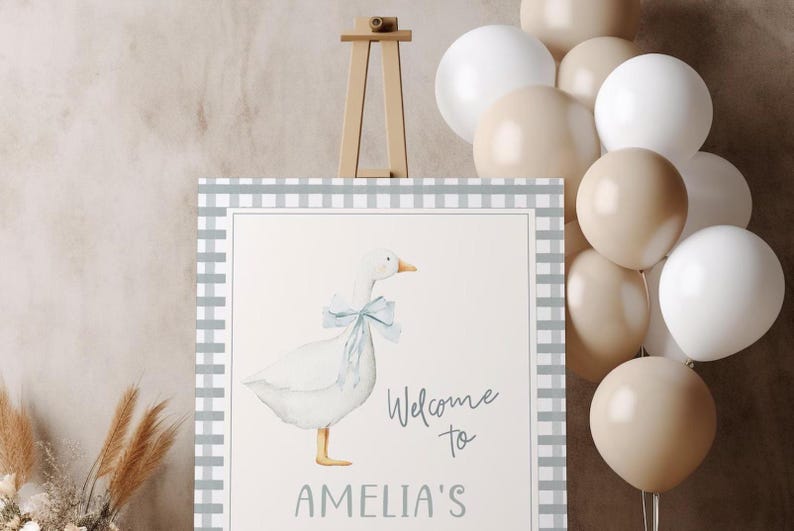 May include: A welcome sign with a gray and white checkered border. The sign features a watercolor illustration of a white goose with a blue bow. The text on the sign reads "Welcome to Amelia's".