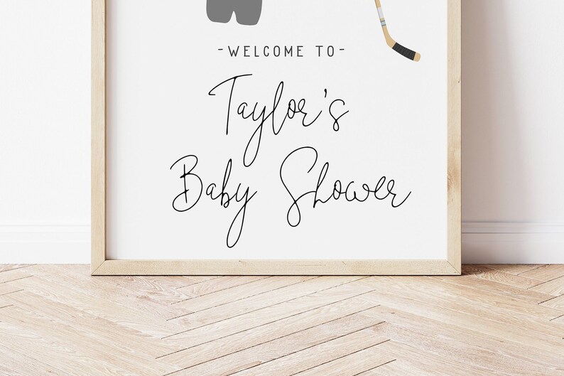 Pode incluir: Uma placa branca emoldurada com texto preto que diz "Bem-vindo ao Chuveiro de Beb&ecirc; de Taylor". Um taco de h&oacute;quei e um par de patins de gelo s&atilde;o ilustrados em cinza na placa.