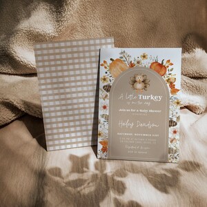 Puede incluir: Una invitaci&oacute;n a un baby shower con una ilustraci&oacute;n de pavo y el texto "A little Turkey is on the way". La invitaci&oacute;n tiene un patr&oacute;n de cuadros beige y blanco en la parte posterior y est&aacute; decorada con calabazas y follaje de oto&ntilde;o.