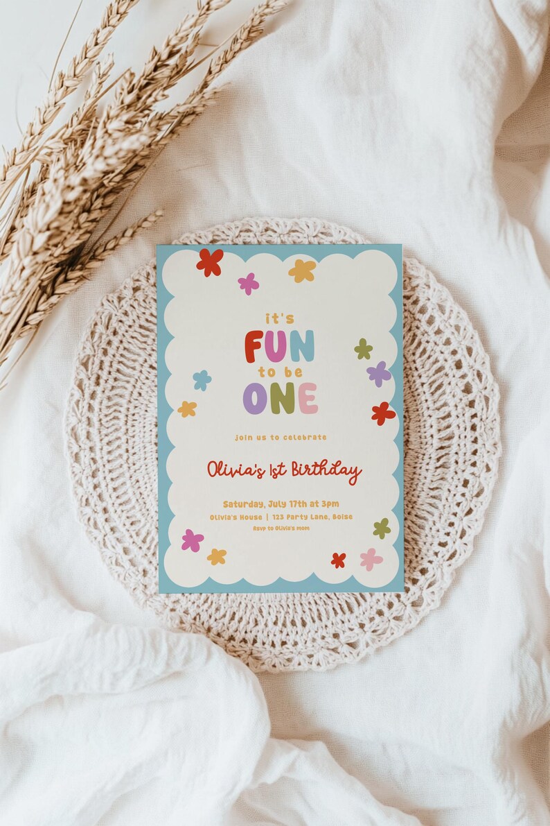 May include: A light blue birthday invitation with a scalloped edge, featuring the text "it's FUN to be ONE" in colorful letters. The invitation includes details for Olivia's 1st birthday, surrounded by flower illustrations.