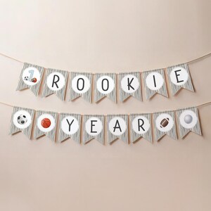May include: A black and white striped banner with the words "Rookie Year" and sports-themed icons. The banner is strung on a white wall.