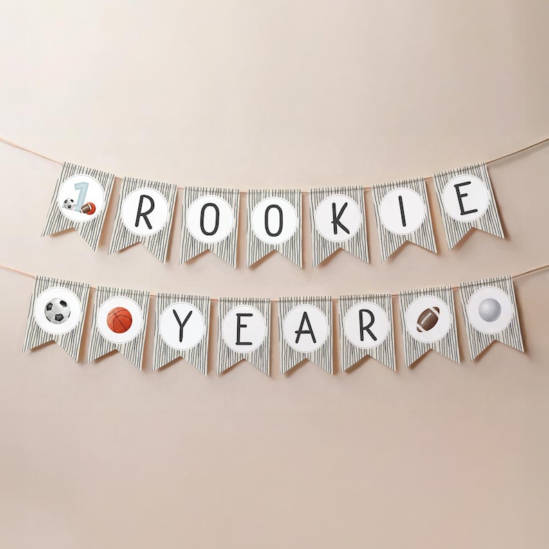 May include: A black and white striped banner with the words "Rookie Year" and sports-themed icons. The banner is strung on a white wall.