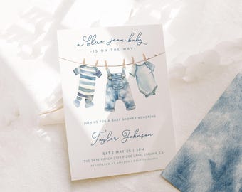 May include: A baby shower invitation with a blue watercolor design. The invitation says "a blue jean baby - is on the way -" and features a line of clothes hanging on a clothesline. The clothes include a blue and white striped onesie, a pair of blue jean overalls, and a light blue onesie. The invitation also includes the name "Taylor Johnson", the date "Sat | May 26 | 3PM", the location "The Skye Ranch | 129 Ridge Lane, Laguna, CA", and the registry information "Registered at Amazon RSVP to Olivia."