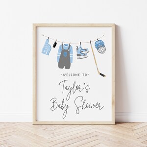 Pode incluir: Um cartaz branco com um an&uacute;ncio de ch&aacute; de beb&ecirc; de h&oacute;quei em azul e cinza. O cartaz diz "Bem-vindo ao ch&aacute; de beb&ecirc; de Taylor".