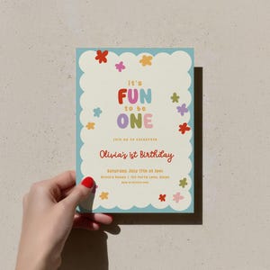 May include: A colorful birthday invitation with a light blue scalloped border. The text "It's FUN to be ONE" is displayed in vibrant colors. The invitation also includes the text "Olivia's 1st Birthday" and event details. Floral accents are scattered around the design.