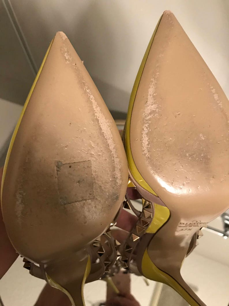 May include: A pair of yellow high-heeled shoes with gold studs. The shoes have a pointed toe and a thin strap across the foot. The soles of the shoes are beige.