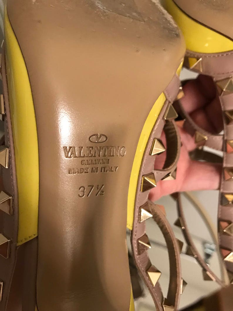 May include: Close-up of the bottom of a yellow and beige high-heeled shoe with gold studs. The shoe is labeled "VALENTINO GARAVANI MADE IN ITALY" and "37 1/2".