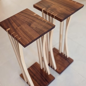 May include: Two wooden side tables with a walnut top and a light wood base. The base is made of multiple thin strips of wood that are curved and interlocked.
