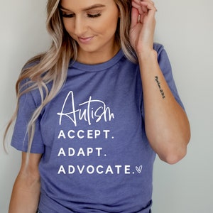 May include: A woman wearing a purple t-shirt with the text "Autism ACCEPT. ADAPT. ADVOCATE." in white lettering.