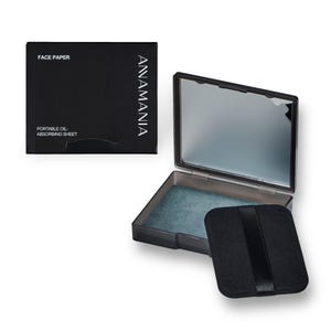 May include: A black compact with a mirror and a black felt pad inside. The compact has the text "ANNAMANIA" printed on the side and "FACE PAPER" and "PORTABLE OIL ABSORBING SHEET" printed on the top.