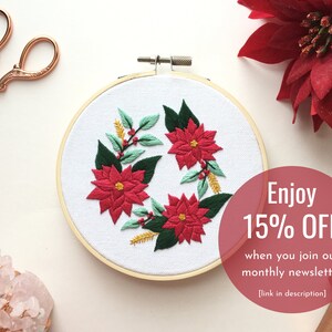 May include: Embroidered hoop art featuring a wreath of poinsettia flowers and greenery. The hoop is wooden and the background is white. The text "Enjoy 15% OFF when you join our monthly newsletter [link in description]" is visible in the lower right corner.
