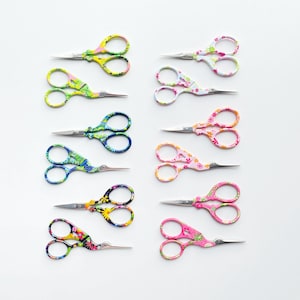 May include: Ten small embroidery scissors with floral patterns in various colours. The scissors have silver blades and loop handles. The floral patterns include yellow, green, blue, pink, and black. Each pair is designed for detailed craft work.