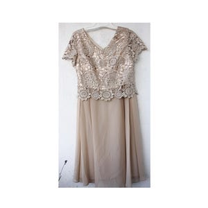 May include: A beige lace dress with a chiffon skirt. The dress has a V-neckline and short sleeves.