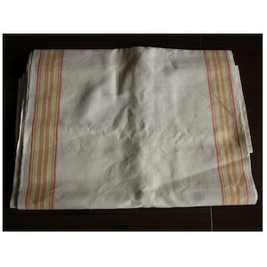 Pode incluir: Uma toalha de cozinha de linho branco com listras laranja e amarelas nas bordas.