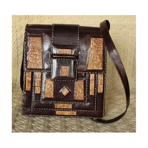 May include: A brown leather shoulder bag with a geometric design. The bag is made of different pieces of leather, some of which are a light brown color. The bag has a flap closure and a long strap.