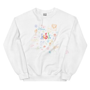 May include: White sweatshirt with a colourful doodle design featuring the word "hibli" and various images, including a flower, a heart, a glass of wine, a bag, and a pair of sandals.