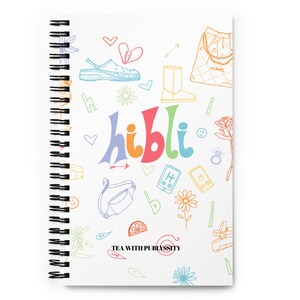 May include: A white spiral bound notebook with a colourful doodle design. The notebook features the word "hibli" in rainbow colours and various doodles including hearts, flowers, a purse, a boot, a phone, and a lemon. The text "TEA WITH PUBSISSITY" is printed at the bottom of the notebook.