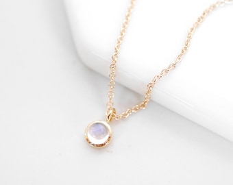 May include: A delicate gold chain necklace with a small, round moonstone pendant.