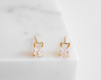 May include: A pair of gold earrings with clear square-shaped cubic zirconia stones.